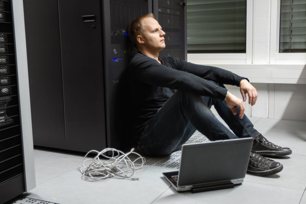 Hochverfügbarkeit in der IT: Frustrierter auf dem Boden vor einem Server sitzender IT Techniker